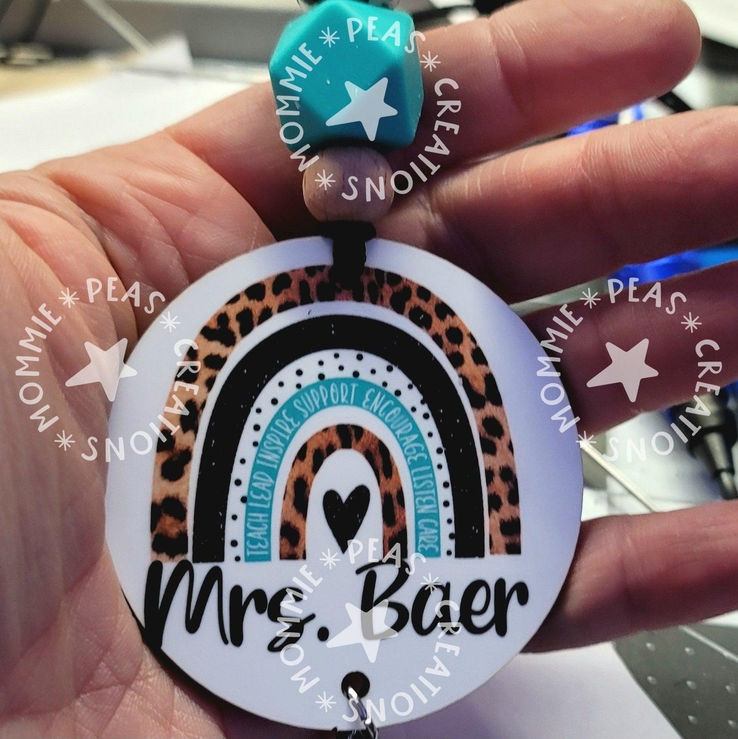 Hand holding a round keychain with leopard print and black rainbow design, text 'Mr. Baer'