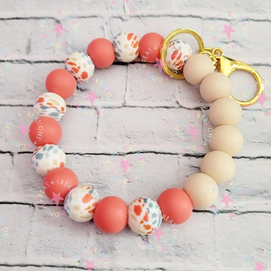 Handmade beaded keychain bracelet with coral, cream, and multicolor beads, gold clasp