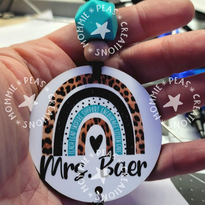 Hand holding a round keychain with leopard print and black rainbow design, text 'Mr. Baer'