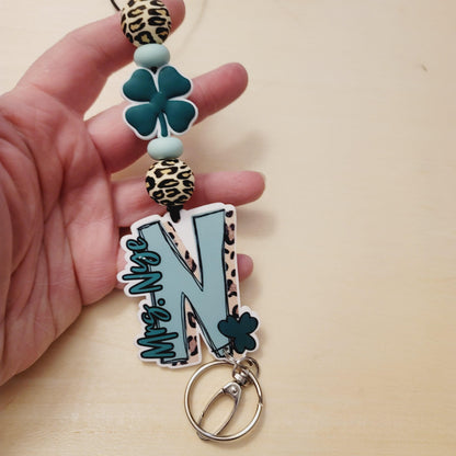 Hand holding a keychain with teal four-leaf clover, leopard print beads, and teal letter N charm