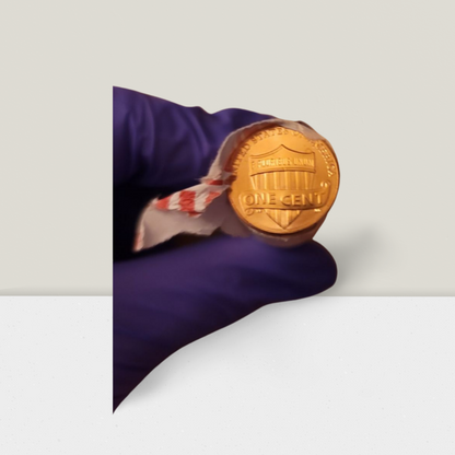 Hand holding shiny copper penny roll with purple glove, handmade gift item background.