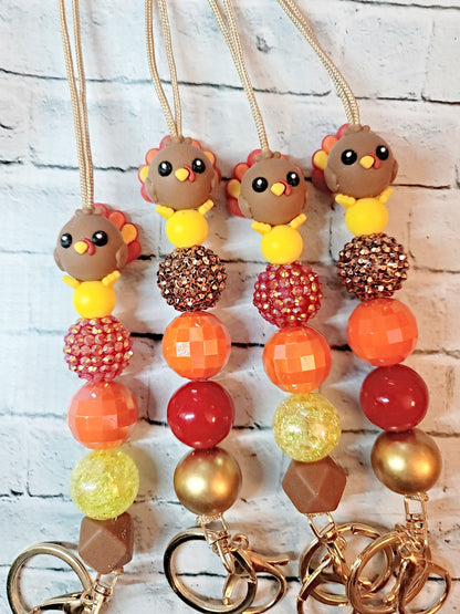 a collection of colorful beaded keychains with small turkey-like figures on them, arranged on a white brick background.