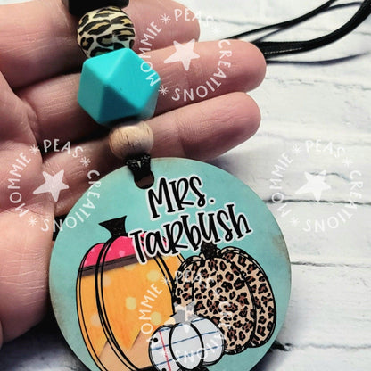 Hand holding a keychain with colorful beads and a round tag featuring pumpkins and 'Mrs. Tarbush' text