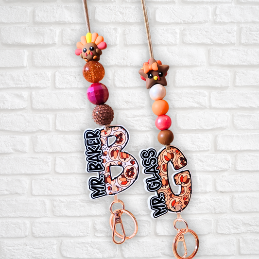 two colorful keychains hanging on a white brick wall.