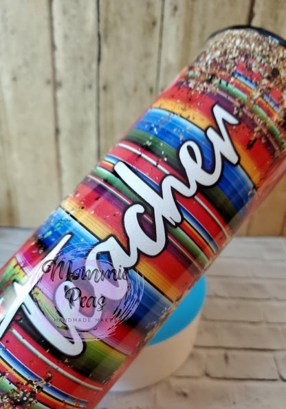 Colorful tumbler with Mexican-style striped pattern and white text saying 'teacher' sprinkled with glitter