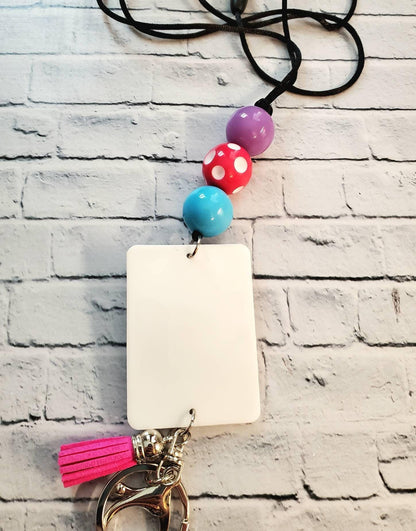 Colorful beaded lanyard with purple, red polka dot, and blue beads, white ID card, pink tassel, and key clasp on white brick background
