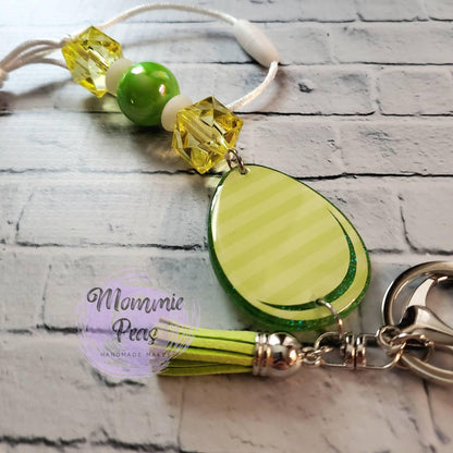 Green and yellow keychain with beads and a striped teardrop pendant on white brick background
