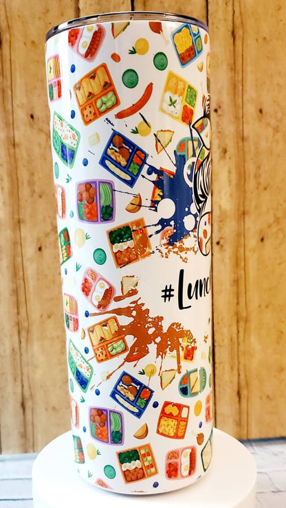 White tumbler with colorful lunchbox and food illustrations, wooden background