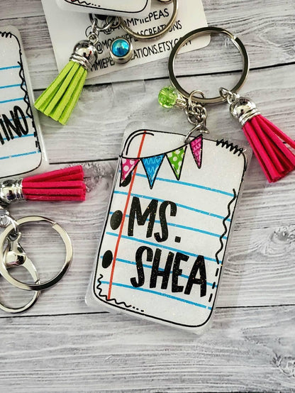 Personalized Ms. Shea teacher keychain with colorful tassel and decorative flags on wooden background
