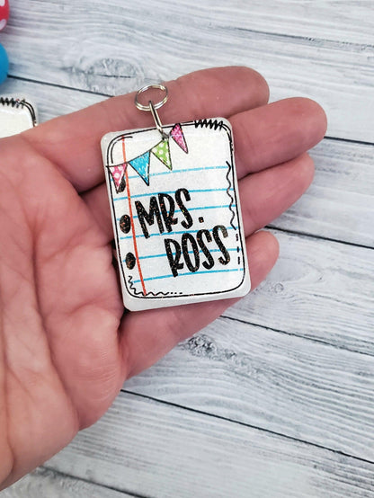 Hand holding Mrs. Ross keychain with notebook paper design and colorful flags