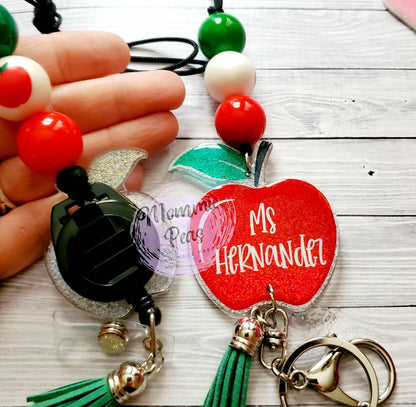 Personalized apple-shaped badge reel and keychain with Ms Hernandez text, green tassels, and colorful beads