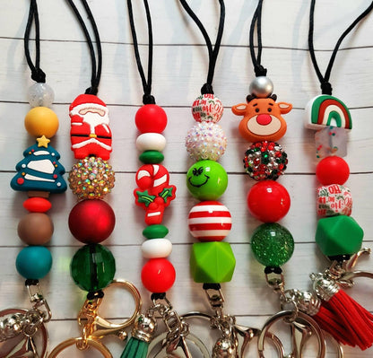 Six Christmas-themed keychains with beads and festive charms including tree, Santa, candy canes, Grinch, reindeer, and rainbow.