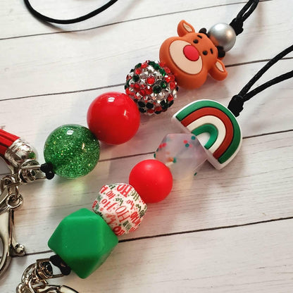 Christmas-themed keychains with beads, including a reindeer face and rainbow charm on white wood background