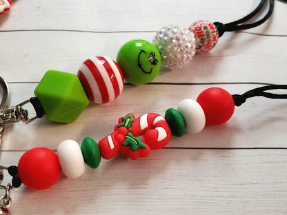 Christmas-themed keychains with colorful beads, candy cane charm, and smiley face bead on white wooden surface