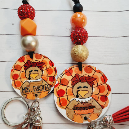Hand-painted turkey keychains with red, orange, gold beads and personalized name on white wooden background