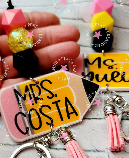 Personalized pencil-shaped keychains with names Ms. Costa and Ms. Suel, featuring colorful beads and pink tassels