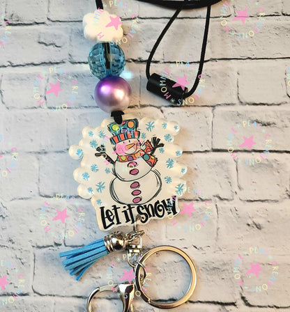Holiday keychain with smiling snowman illustration, blue tassel, beads, and Let It Snow text