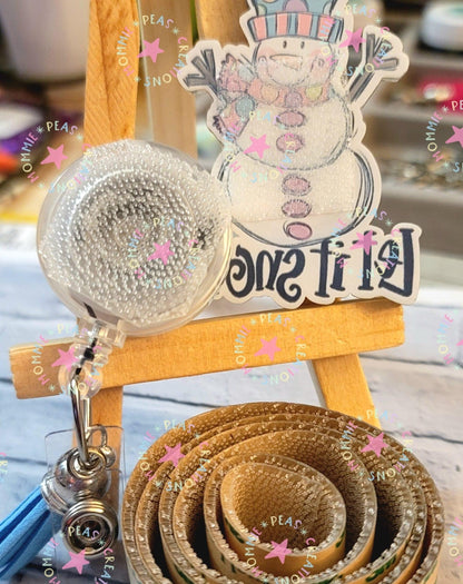 Retractable badge reel with a measuring tape and snowman sticker on a small wooden easel