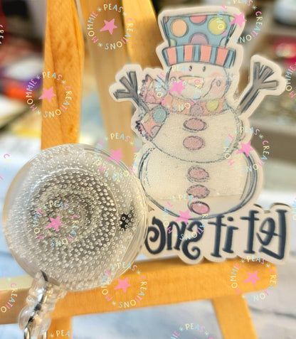 Clear badge reel with water droplets in front of a smiling snowman illustration on a wooden easel