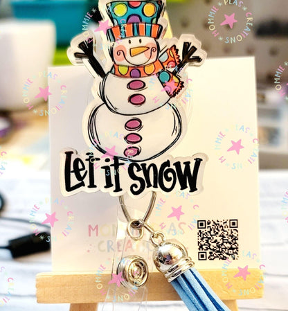 Colorful snowman keychain with Let it Snow text and blue tassel on display stand