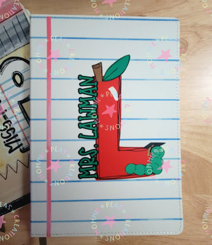 Lined notebook cover with large red 'L' apple design and text Mrs. Laiman with green worm wearing graduation cap