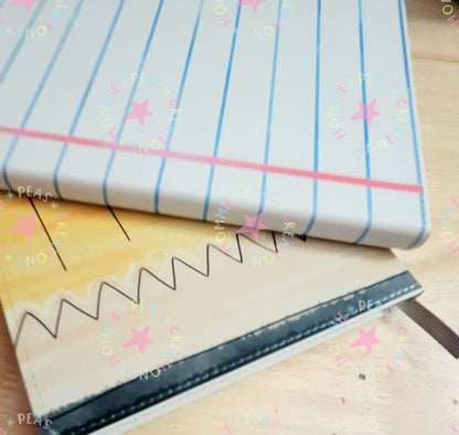 Close-up of a fabric notebook cover with blue lines and a pink border, resting on a wooden table