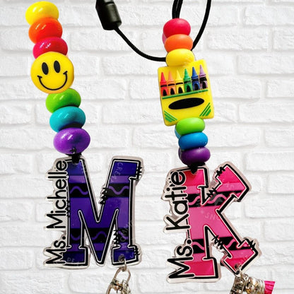 Colorful personalized teacher lanyards with smiley face and crayon beads, names Ms. Michelle and Ms. Katie