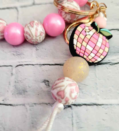 Pink and white beaded keychain with mosaic apple charm on gray brick background