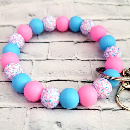 Round keychain bracelet with pink, blue, and multicolor patterned beads on white brick background