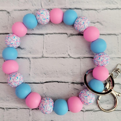 Beaded wrist keychain with pink, blue, and patterned round beads on white brick background