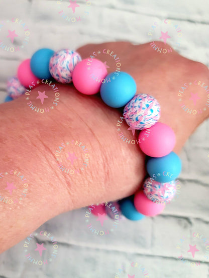 Close-up of pink and blue beaded bracelet with speckled beads on wrist over light brick background