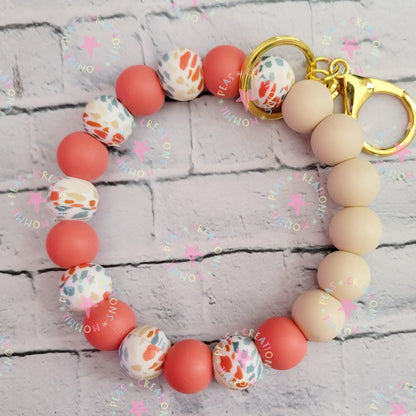 Silicone bead keychain bracelet with peach, beige, and patterned beads on gold rings