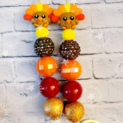 Colorful turkey-themed beaded keychain with orange, red, yellow, and gold round beads on white brick background