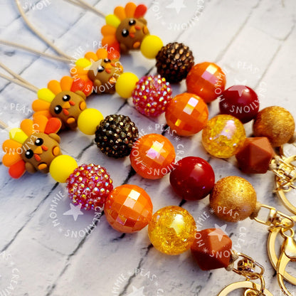 Colorful beaded keychains with turkey charms in fall colors on a light wooden surface