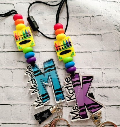 Colorful personalized teacher keychains with blue M and purple K initials and crayon beads on black cords