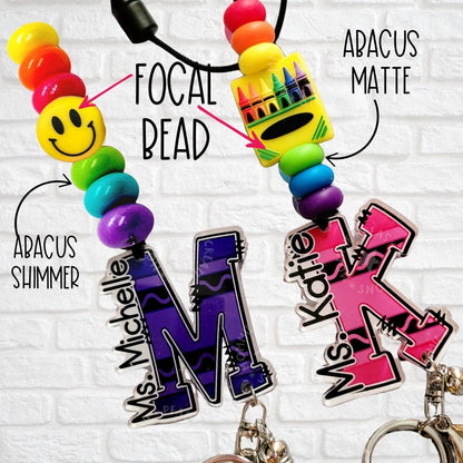Colorful personalized keychains with name tags, abacus beads, and smiley focal bead on a white brick wall