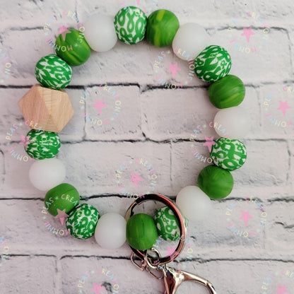 Green and white beaded keychain with a natural wood bead on a light gray brick background