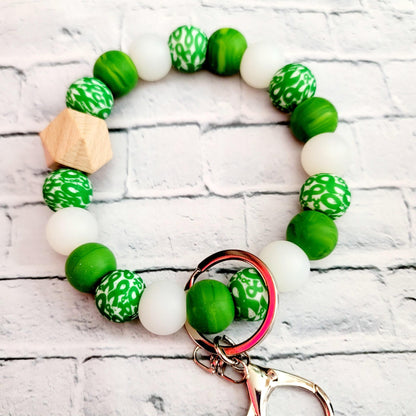 Beaded green and white wristlet keychain with a wooden bead and silver clasp on white brick background