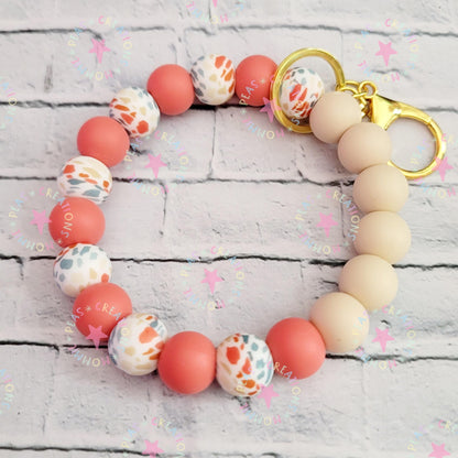 Colorful round silicone bead keychain with gold clasp on white brick background
