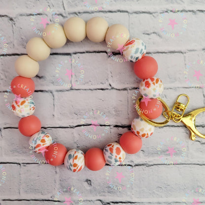 Colorful beaded keychain bracelet with gold clasp on white textured brick background