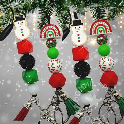 Christmas-themed keychains with snowman and rainbow charms, festive beads, and tassels on pine branch