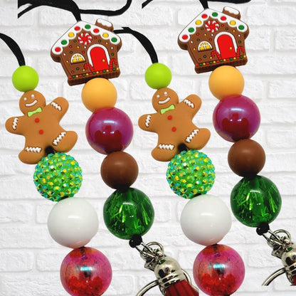 Colorful Christmas-themed keychains with gingerbread men, gingerbread houses, and bright beads on white brick background
