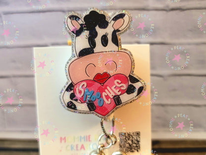 Cute black and white cow badge reel holding pink heart with '6 Moo Oches' text