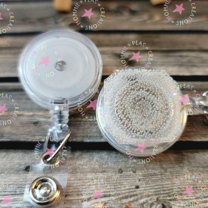 Transparent retractable badge reels with metal clips on wooden surface, one with bubble-covered tape