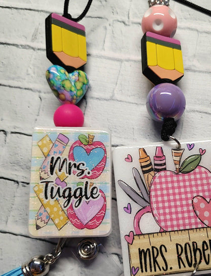 Colorful teacher badge reel with pencil, heart beads, and Mrs. Tuggle text on a brick background
