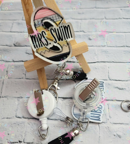 Two badge reels on a white wooden surface, one personalized with a colorful 'Mrs. Swim' tag and black tassel