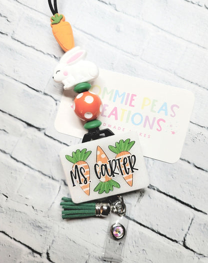 Personalized badge reel with carrots, white bunny, orange polka dot bead, and green tassel on brick background