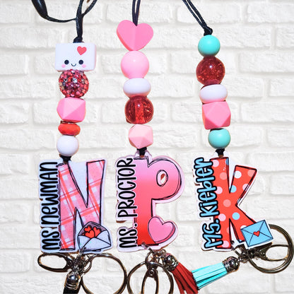 Three personalized Valentine-themed keychains with names Ms Newman, Ms Proctor, Ms Kiepper and decorative beads