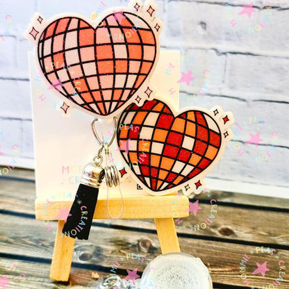 Heart-shaped disco ball keychain with red and orange checkered pattern on small wooden easel