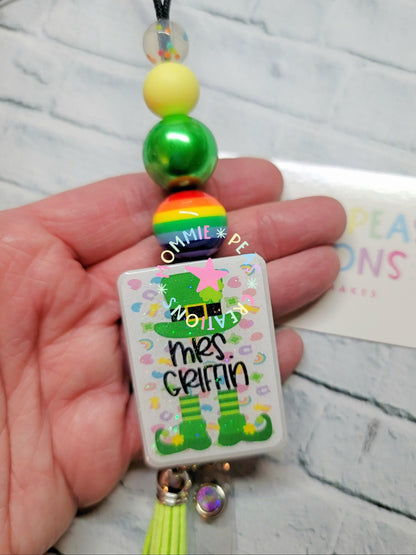 Hand holding a colorful beaded badge reel with a leprechaun design and text Mrs. Griffin